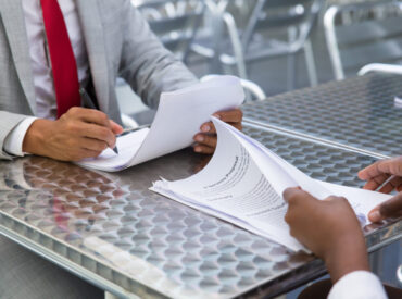 Business partners checking and signing document Business partners checking and signing documents in street cafe. Closeup of papers and writing business man hand. Deal or paperwork concept