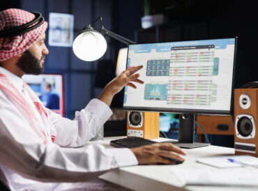 An Arab businessman diligently analyzing data on his computer, making important decisions for the company. Muslim guy wearing traditional attire is checking charts and data on his desktop pc.